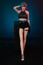 Briana Small Flat Chested Sex Doll with colorful hair, stylish outfit, and high heels, standing confidently in a dark studio setting.