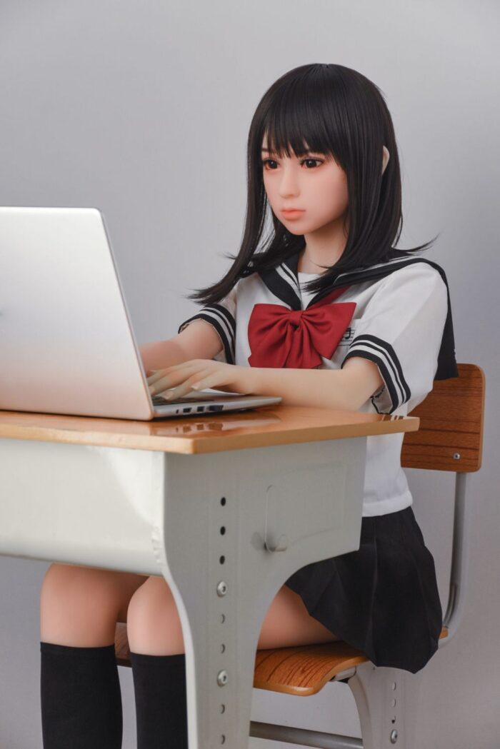 Realistic Sex Doll In Schoolgirl Outfit Using A Laptop, Emphasizing Discreet Pleasure Products For Adults. Perfect For Those Seeking Intimate Companions With A Young, Playful Appearance.