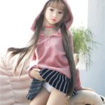 High-quality sex doll miniature girl in pink hoodie and striped skirt, realistic doll for adult companionship, detailed features, soft skin, and lifelike appearance for intimate realism.