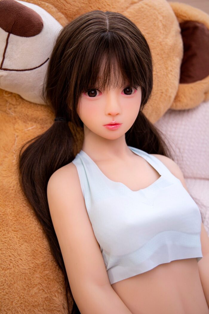 Realistic Sex Doll Female With Long Brown Hair, Lying On A Cozy Bed With Plush Stuffed Animals, Showcasing Detailed Features And High-Quality Craftsmanship For Adult Pleasure And Companionship.