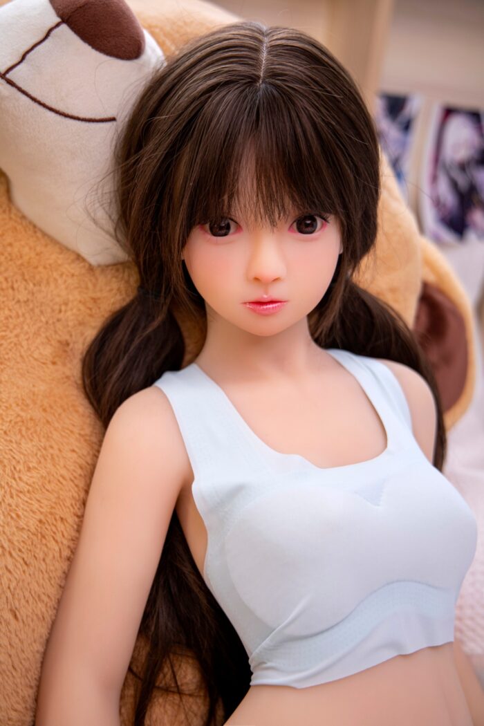 Realistic Sex Doll With Long Brown Hair, Wearing A White Tank Top, Lying On Plush Blanket With Teddy Bear. Perfect For Intimate Companionship And Realistic Experience.