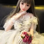Vysokokvalitná sexuálna bábika s realistickými črtami, oblečená v elegantných šatách, s dlhými hnedými vlasmi, kvetinovými doplnkami a šperkami pre sofistikovaný vzhľad. Ideálna pre zberateľov a nadšencov.