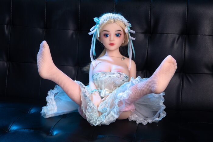 Søt realistisk sexdukke med blondt hår, blå øyne og en detaljert hvit kjole, poserer forførende på en svart sofa, og viser frem det høykvalitets håndverket til Sexdollmini.