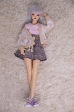 Yumuşak silikon seks bebeği, peluş krem halının üzerinde uzanıyor, gerçekçi özellikler, detaylı kıyafetler, mavi saç aksesuarları, samimi yetişkin arkadaşlığı için modern ve sevimli görünüm, koleksiyoncular ve gerçekçi bebek severler için ideal.