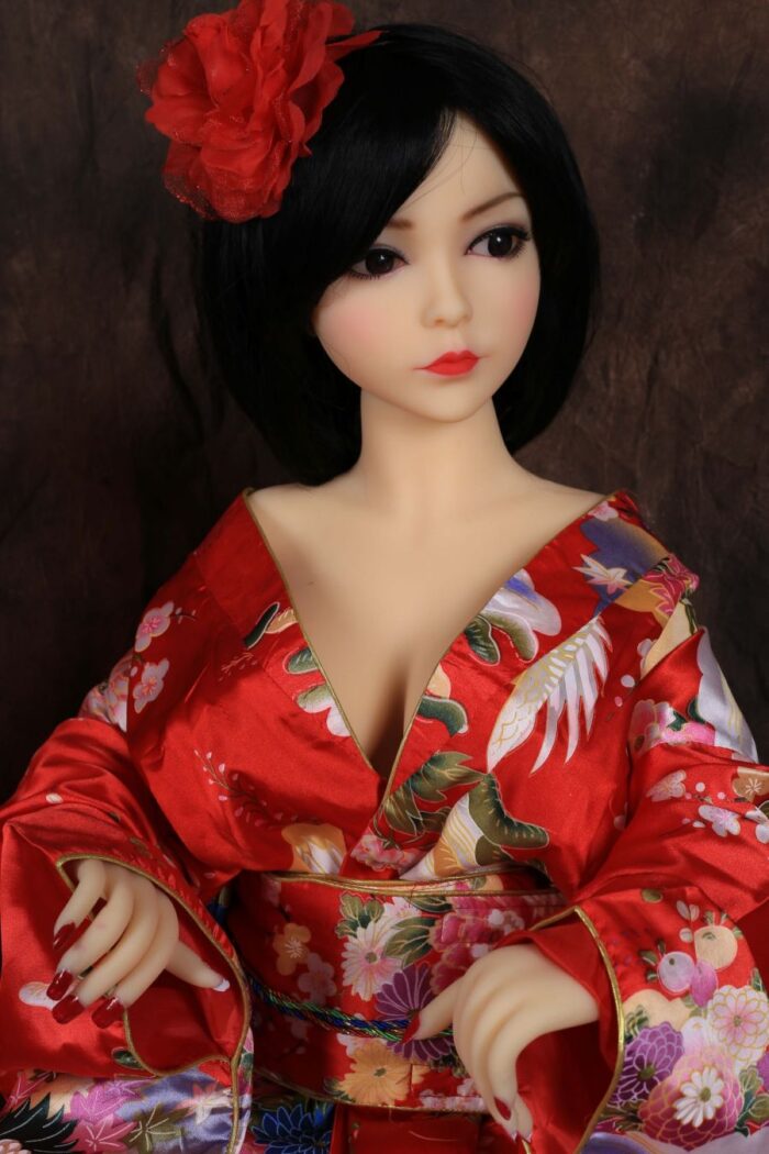 Realistic Japanese-Style Love Doll Wearing A Vibrant, Traditional Kimono With Floral Patterns And A Striking Red Flower Hair Accessory. The Doll Features Detailed Facial Features, Long Black Hair, And A Captivating Gaze.
