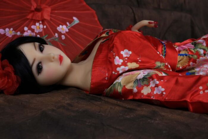 Realistic Sex Doll In Traditional Red Kimono With Floral Patterns, Lying On A Wooden Surface With A Japanese Parasol In The Background, Designed For Intimate Pleasure And Companionship.