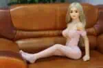 Realistic sex doll sitting on a vintage leather sofa, dressed in a pink lace lingerie dress and fishnet stockings, designed for intimate companionship and sensory pleasure.