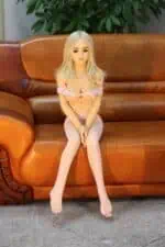 Realistic sex doll sitting on a brown leather sofa, dressed in a revealing pink outfit with lace stockings, offering a lifelike appearance for companionship and adult entertainment.