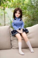 Realistic sex doll female figure with brown hair in a blue school uniform sitting outdoors on a beige sofa. Suitable for adult intimacy, companionship, and collectible purposes, crafted with high-quality materials for lifelike realism.