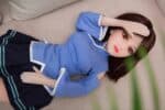 Realistic sex doll female mannequin wearing a blue school uniform on a beige sofa, showcasing detailed features and lifelike appearance for adult pleasure and companionship.