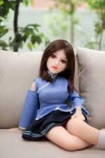 Realistic sex doll with lifelike features, dressed in a blue school uniform, sitting on a sofa in a cozy indoor setting. Perfect for companionship and intimate experiences.