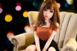 Realistic sex doll sitting on a beige armchair with colorful blurred lights in the background, showcasing high-quality craftsmanship and lifelike features for adult intimacy pleasure.