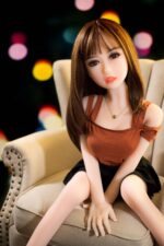 Silicone sex doll with realistic facial features posing on a beige armchair, showcasing high-quality craftsmanship for optimal pleasure and companionship. Perfect for adult intimacy and collector interest.