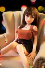 Realistic love doll sitting on an armchair with festive string lights, showcasing a high-quality, lifelike sex doll perfect for adult pleasure and companionship.