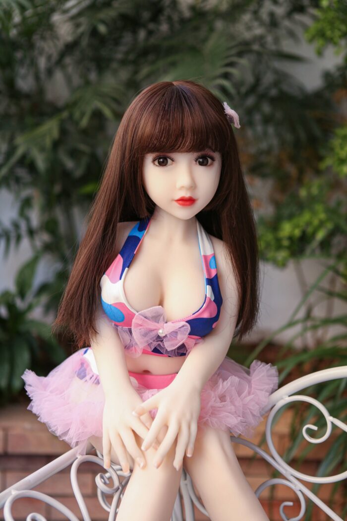 Realistic Sex Doll With Detailed Facial Features And Long Brown Hair, Dressed In A Colorful Bikini Top And Pink Tutu, Posing Outdoors For Lifelike Intimacy Experience.