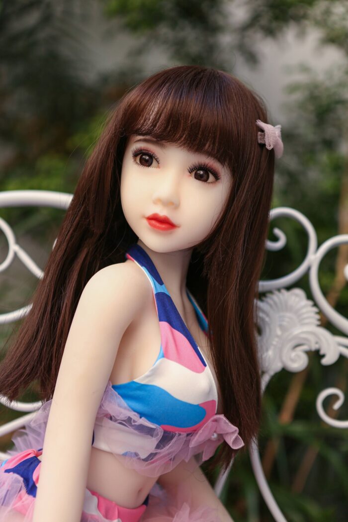 Silicon Sex Doll With Realistic Facial Features, Long Brown Hair, And Detailed Eyes, Dressed In Colorful Clothing, Outdoors Setting, Perfect For Companionship And Adult Pleasure.