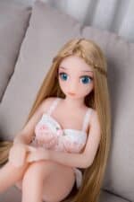 Realistic love doll with long blonde hair, blue eyes, and detailed facial features, posing on a neutral gray couch wearing a lace dress for a premium adult experience.