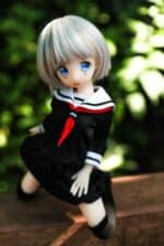 Söpö anime-tyylinen seksinukke sinisilmäisillä japanilaisessa koulutytön asussa ulkona rehevän vihreän lehtien keskellä.