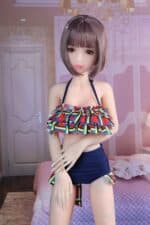 Realistische Sexpuppe mit kurzen braunen Haaren und einem bunten Bikinioberteil mit Rüschen, posiert in einer Schlafzimmerumgebung für intimes Vergnügen. Perfekt für Liebhaber von Sexspielzeug, die lebensechte Begleiter suchen.