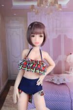 Realistische Sexpuppe mit kurzer Bobfrisur in einem farbenfrohen Rüschenbadeanzug in einem luxuriösen Schlafzimmer.