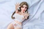 Realistic sex doll with detailed facial features, long braided hair, and a youthful appearance, lying on a soft bed, designed for adult pleasure. Perfect for intimate companionship.