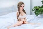 Realistic sex doll on a white bed with long braided hair, wearing a cute tank top, in a modern bedroom setting designed for adult pleasure and companionship.