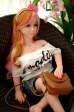 Weiche Silikon-Sexpuppe mit realistischen Gesichtszügen und langem, buntem Haar, sitzt in einem Korbstuhl mit rosa Blumen in der Nähe und präsentiert lebensechtes Design und anpassbare Optionen.