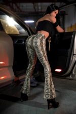 Boneca sexual Arcadia Petite Angel feita de TPE, vestindo um elegante top preto e calças com estampa de cobra em um estacionamento.