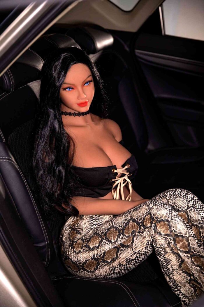 Boneca sexual realista com longos cabelos pretos, olhos azuis e pernas com estampa de cobra, sentada em uma cadeirinha de carro.
