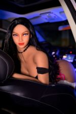 Boneca sexual realista Arcadia Petite Angel em TPE com longos cabelos pretos e olhos azuis, posando dentro de um carro para uma sessão de fotos sensual.