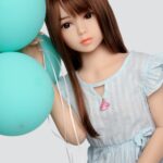 Realistic sex doll with a youthful appearance holding teal balloons, soft facial features, long brown hair, and dressed in a light blue dress, designed for adult pleasure and companionship.