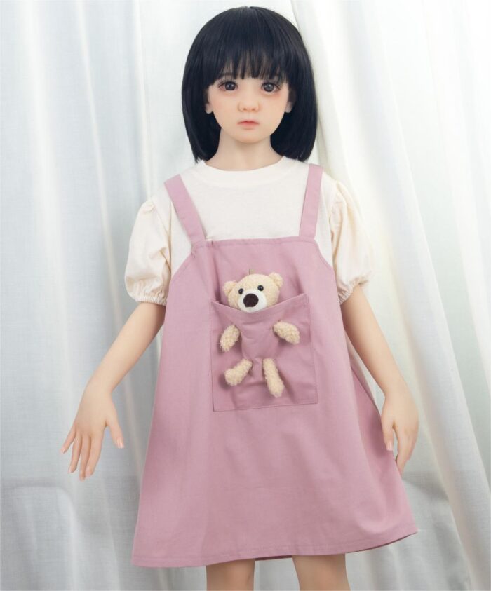 Fleur Sex Doll3 Anime Girl Doll With Black Hair In Pink Dress Holding Plush Teddy Bear On A Curtain Background.